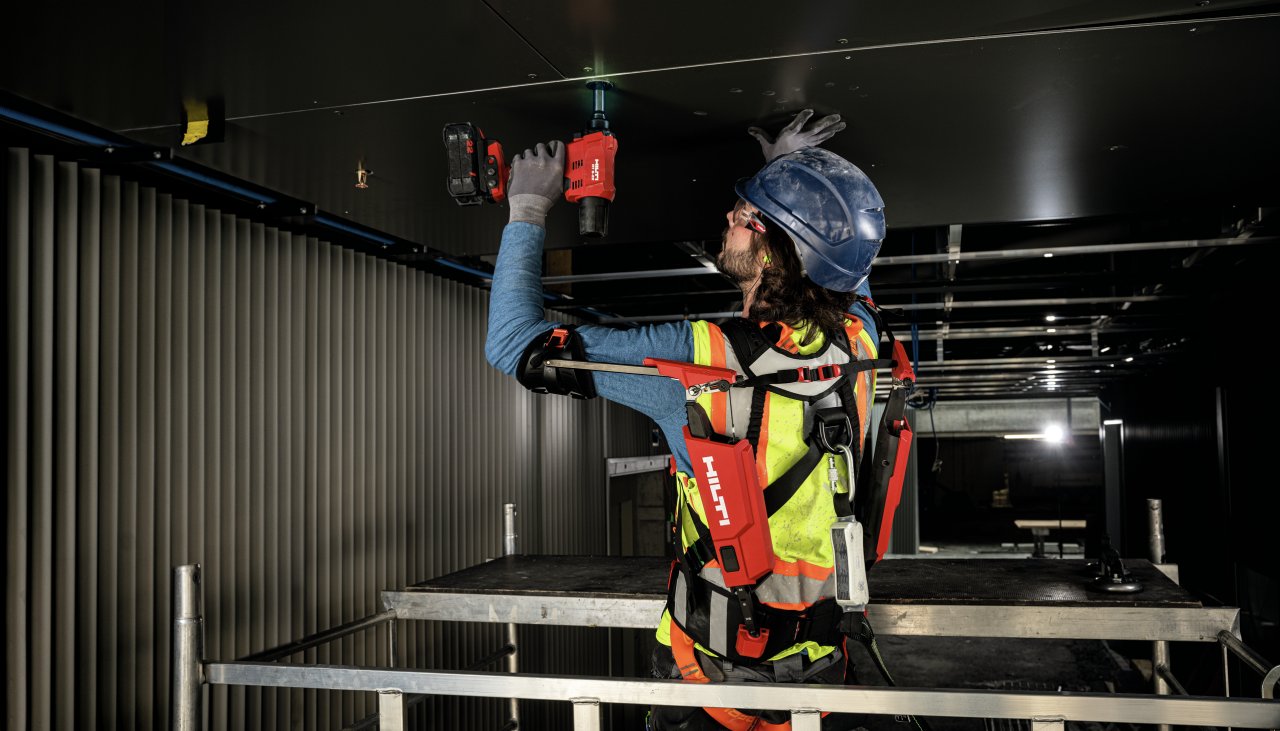 Arbeiter mit Exo-Skelett und Akku-Schrauber bei Deckenarbeiten